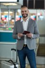 Retrato de un hombre de negocios sonriente con equipaje revisando su tarjeta de embarque en la terminal del aeropuerto - foto de stock