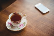 Cup of tea and mobile phone on wooden table at home — Stock Photo