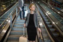 Businesswoman with luggage walking downstairs beside escalator at airport terminal — Stock Photo