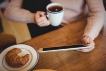 Frau nutzt digitales Tablet während sie Kaffeetasse zu Hause hält — Stockfoto