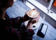 Sezione centrale della donna che tiene in mano una tazza di caffè nel caffè — Foto stock
