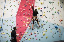 Trainer hilft Frau beim Klettern auf künstliche Wand in Turnhalle — Stockfoto