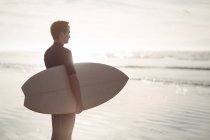Nachdenklicher Surfer steht mit Surfbrett am Strand — Stockfoto