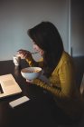 Frau isst Müsli, während sie zu Hause im Arbeitszimmer am Laptop arbeitet — Stockfoto