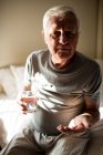 Старший мужчина принимает лекарства в спальне дома — стоковое фото