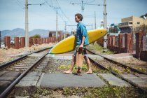 Человек, несущий скейтборд и доску для серфинга при пересечении железнодорожного пути — стоковое фото