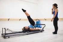 Allenatrice donna che assiste la donna con esercizio di stretching sul riformatore in palestra — Foto stock