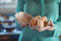 Partie médiane de la femme tenant des œufs dans la cuisine — Photo de stock