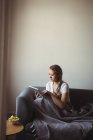 Жінка, використовуючи цифровий планшетний відпочиваючи на диван в домашніх умовах — стокове фото