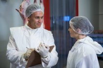 Dos carniceros discutiendo informe en fábrica de carne - foto de stock