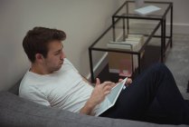 Человек, использующий цифровой планшет на диване дома — стоковое фото