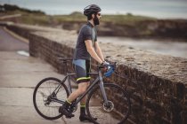 Спортсмен, стоящий с велосипедом на прибрежной дороге — стоковое фото