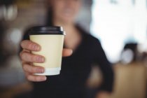 Крупним планом офіціантка стоїть з одноразовою чашкою кави в кафе — стокове фото