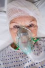 Крупним планом старший пацієнт носить кисневу маску, що лежить на лікарняному ліжку — стокове фото