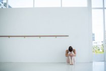 Sad ballerina sitting on floor in ballet studio — Stock Photo