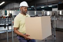 Serious male employee carrying cardboard box in juice factory — Stock Photo