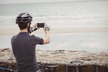 Rear view of athlete taking photo of sea on smartphone — Stock Photo