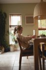 Вид сбоку на девочку, сидящую за столом и читающую книгу дома — стоковое фото