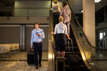 Personal femenino y pasajeros en escaleras mecánicas en el aeropuerto - foto de stock