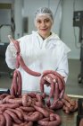 Retrato de açougueiro fêmea segurando salsichas na fábrica de carne — Fotografia de Stock