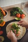 Gros plan des mains masculines plaçant des herbes sur le burrito sur le plan de travail de la cuisine — Photo de stock