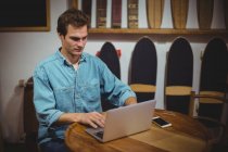 Man using laptop in surfboard and skateboard shop — Stock Photo