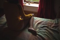 Donna seduta sul letto e guardando attraverso la finestra a casa — Foto stock
