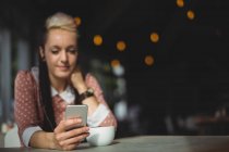 Жінка використовує мобільний телефон, маючи каву в кафе — стокове фото