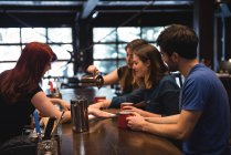 Друзья, держащие кофе за стойкой бара и общающиеся с барменом — стоковое фото