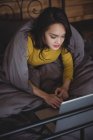 Femme couchée sur le lit en utilisant un ordinateur portable dans la chambre à coucher à la maison — Photo de stock
