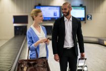 Улыбающаяся пара, идущая со своими тележками в терминале аэропорта — стоковое фото