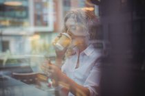 Metà donna d'affari adulta bere caffè e utilizzando il telefono al bancone in caffetteria — Foto stock