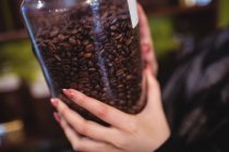 Close-up de mulher segurando jarra de grãos de café no balcão na loja — Fotografia de Stock