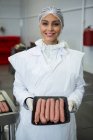 Portrait of female butcher holding tray of sausages at meat factory — Stock Photo