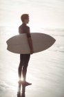 Surfeur réfléchi debout avec planche de surf sur la plage — Photo de stock