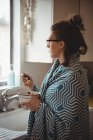Mujer de pie en la cocina comiendo cereales en casa - foto de stock