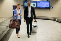 Улыбающаяся пара, идущая со своими тележками в терминале аэропорта — стоковое фото