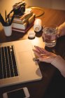Женщина, принимающая лекарства во время работы на ноутбуке дома — стоковое фото