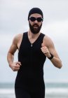 Athlete in swimming goggles running on the beach — Stock Photo