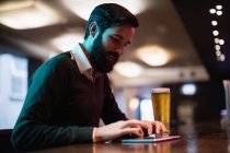 Hombre usando tableta digital con vaso de cerveza en el mostrador en el bar - foto de stock