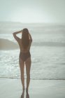 Вид ззаду жінки, що стоїть на пляжі в сонячний день — стокове фото
