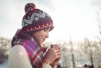 Зимой, во время лыжных каникул, женщина надевает чашку с напитком — стоковое фото