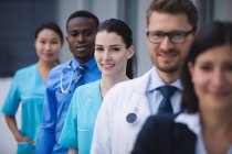 Portrait of smiling doctors standing in row at hospital premises — Stock Photo