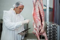 Metzger führt Aufzeichnungen auf digitalem Tablet in Fleischfabrik — Stockfoto