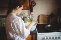 Mujer de pie y sosteniendo un tazón en la cocina en casa - foto de stock