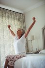 Старшая женщина вытягивает руки на кровати в спальне дома — стоковое фото