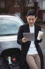 Uomo che utilizza tablet digitale durante la ricarica di auto presso la stazione di ricarica del veicolo elettrico — Foto stock