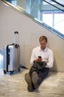 Businessman sitting on floor and using mobile phone in waiting area at airport terminal — Stock Photo