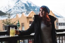 Femme en vêtements d'hiver tenant verre de bière en terrasse extérieure — Photo de stock