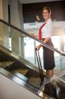 Retrato del personal femenino con equipaje en escaleras mecánicas en el aeropuerto - foto de stock